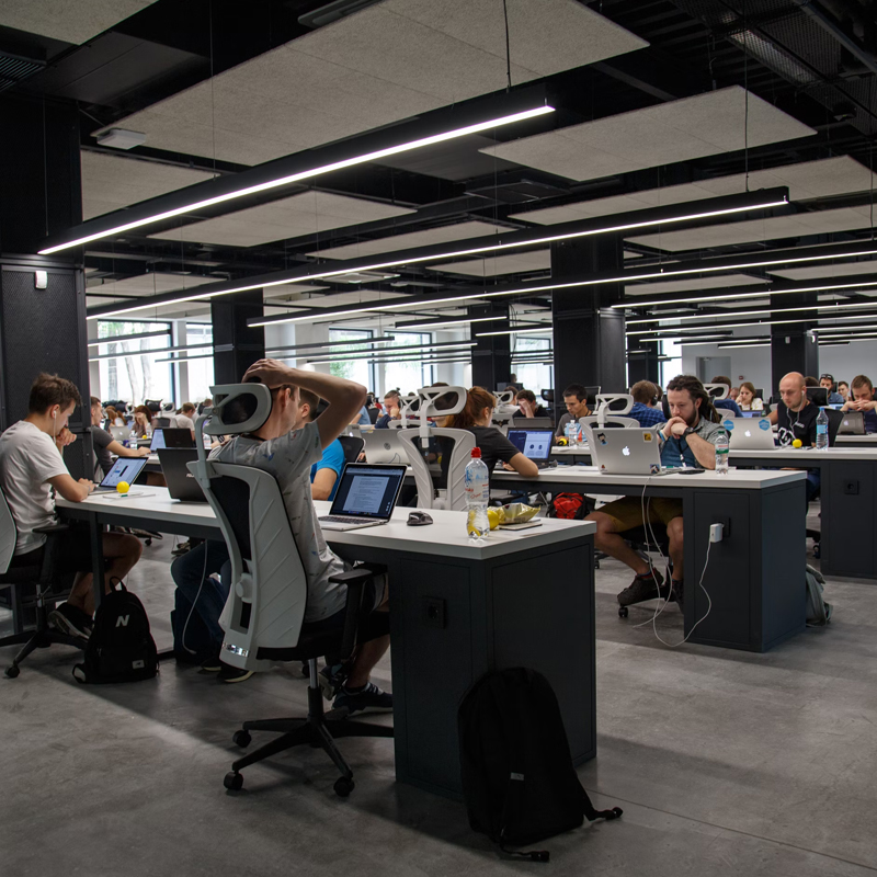 An office space, filled with rows of designs with people working on laptops